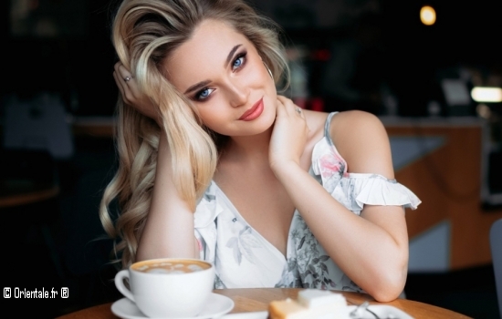 Femme blonde aux yeux bleus attablée Femme blonde aux yeux bleus attablée