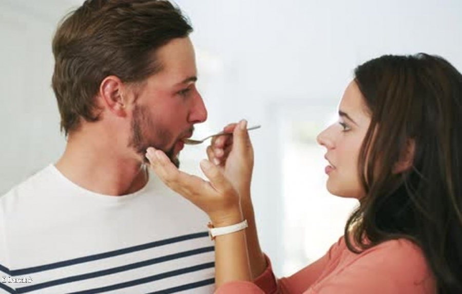 Une femme tend une cuillre  son mari pour le nourrir